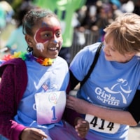 A Girls on the Run coach smiles while holding a program medal at the 5K